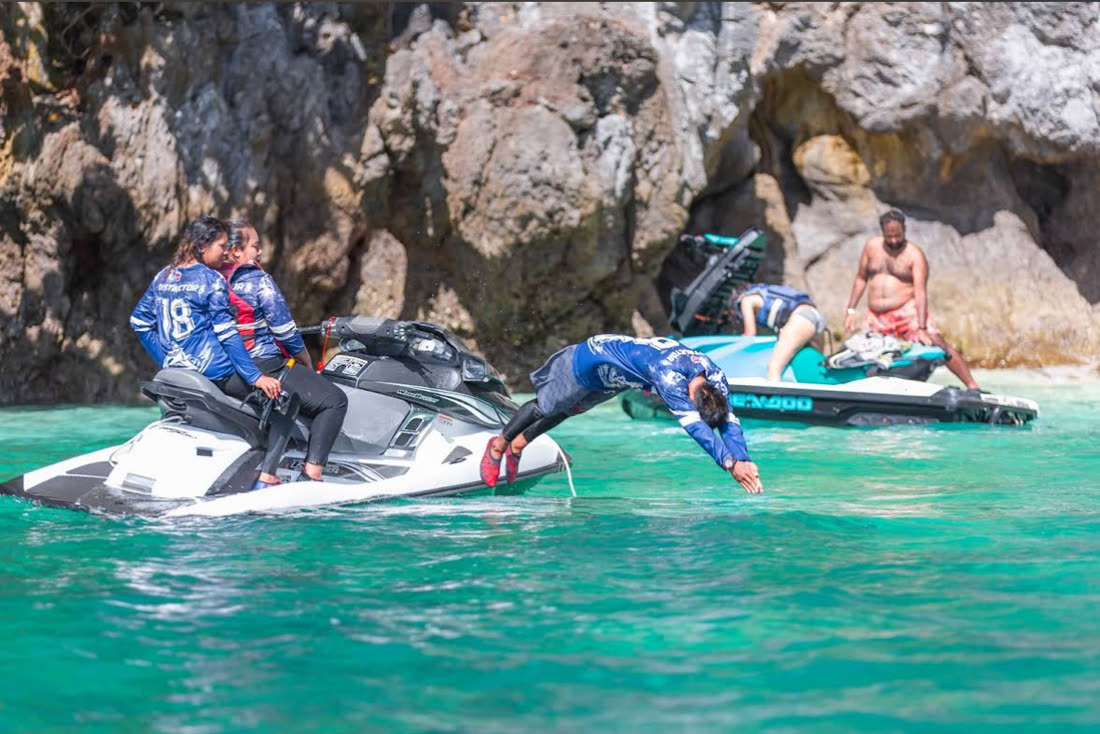 A rider diving off a jet ski beside a cliff